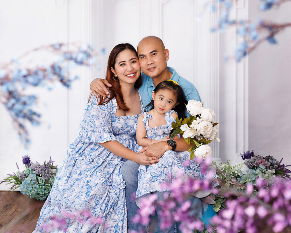 Family portrait of three, wearing floral sky blue with their 7 years old daughter.  Floral theme. 