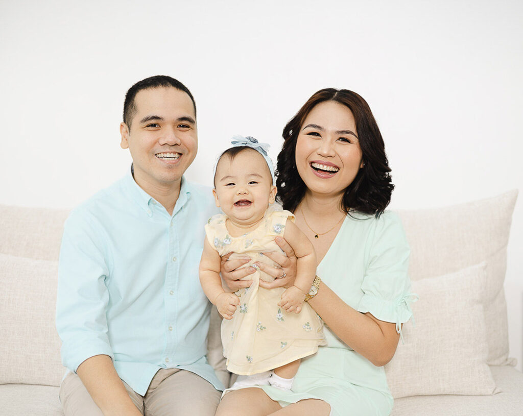 Family photography in the Philippines, a family of three smiling, holding a baby. They are wearing pastel green outfits.